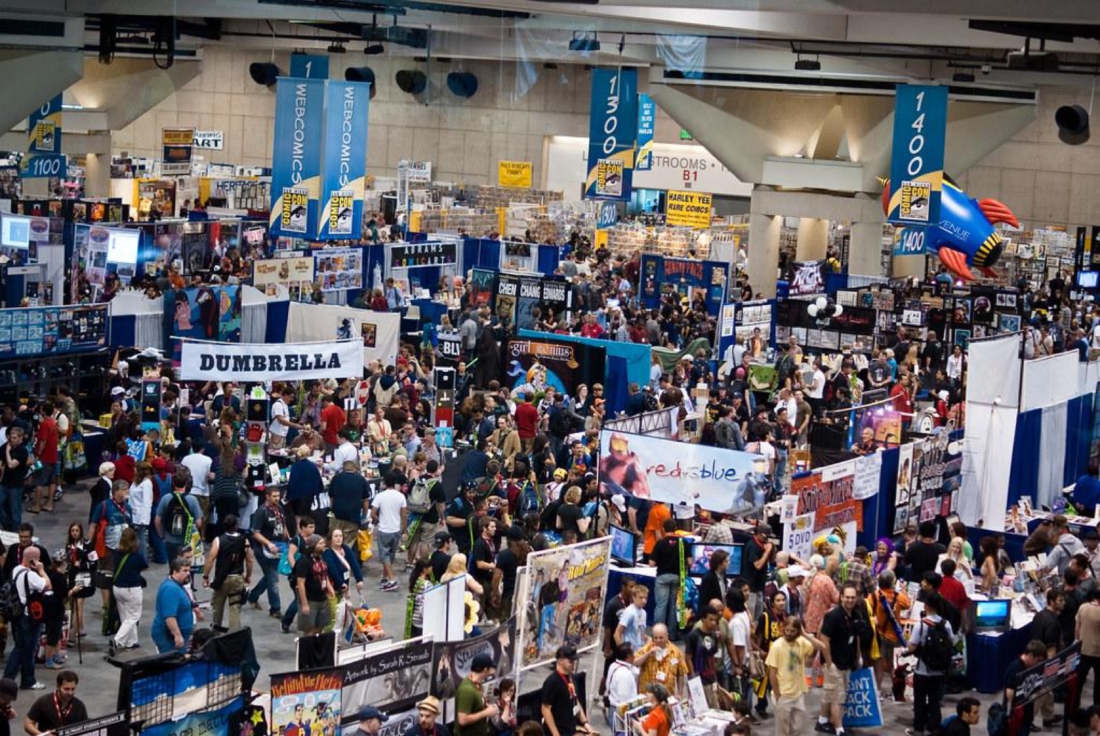 A packed comic convention floor with vendor booths - one of the most common sales channels for self-published books and card games
