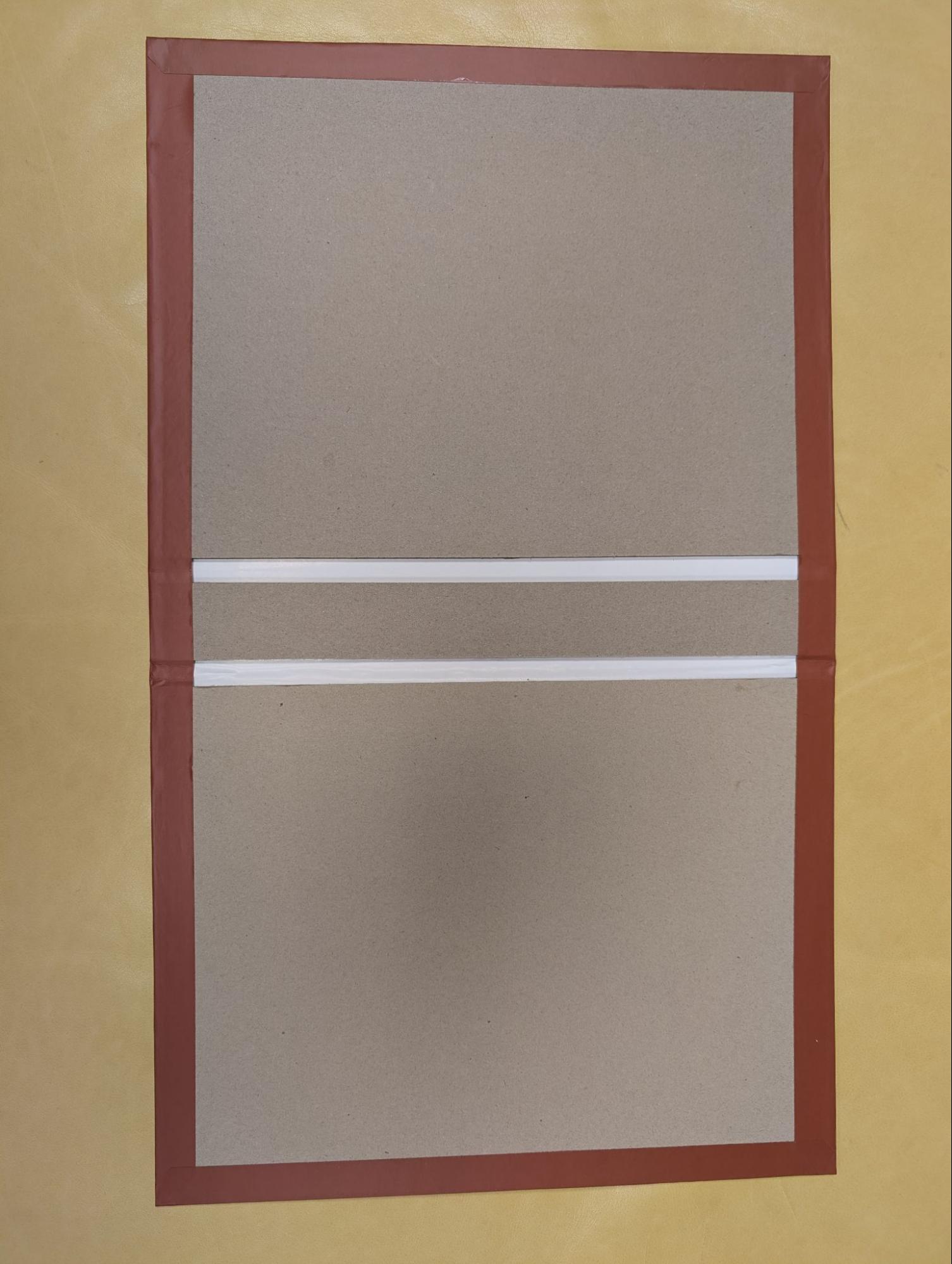 Photograph of an open hardcover case proof showing the red printed cover wrapping over the edge of the chipboard and glued down before endsheets are applied