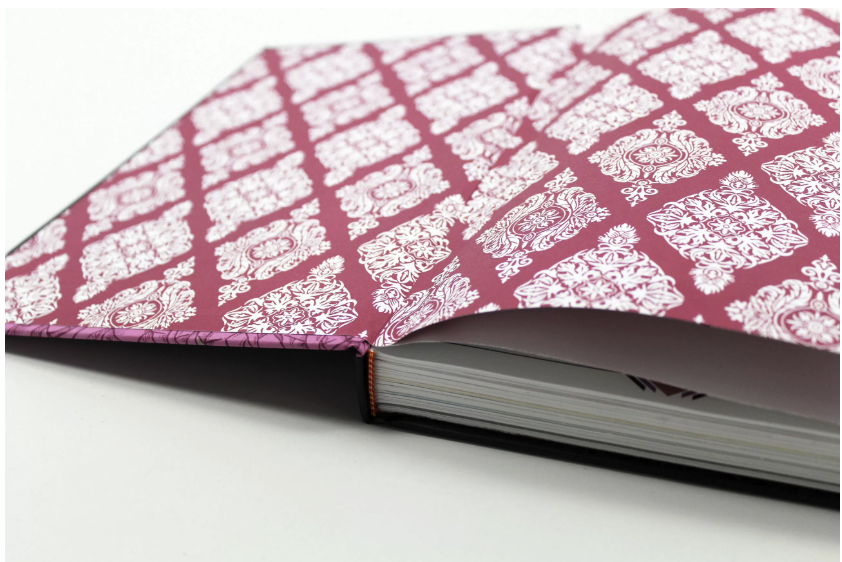 Photograph of an open hardcover book showing patterned magenta separated endsheets between the cover and the interior pages
