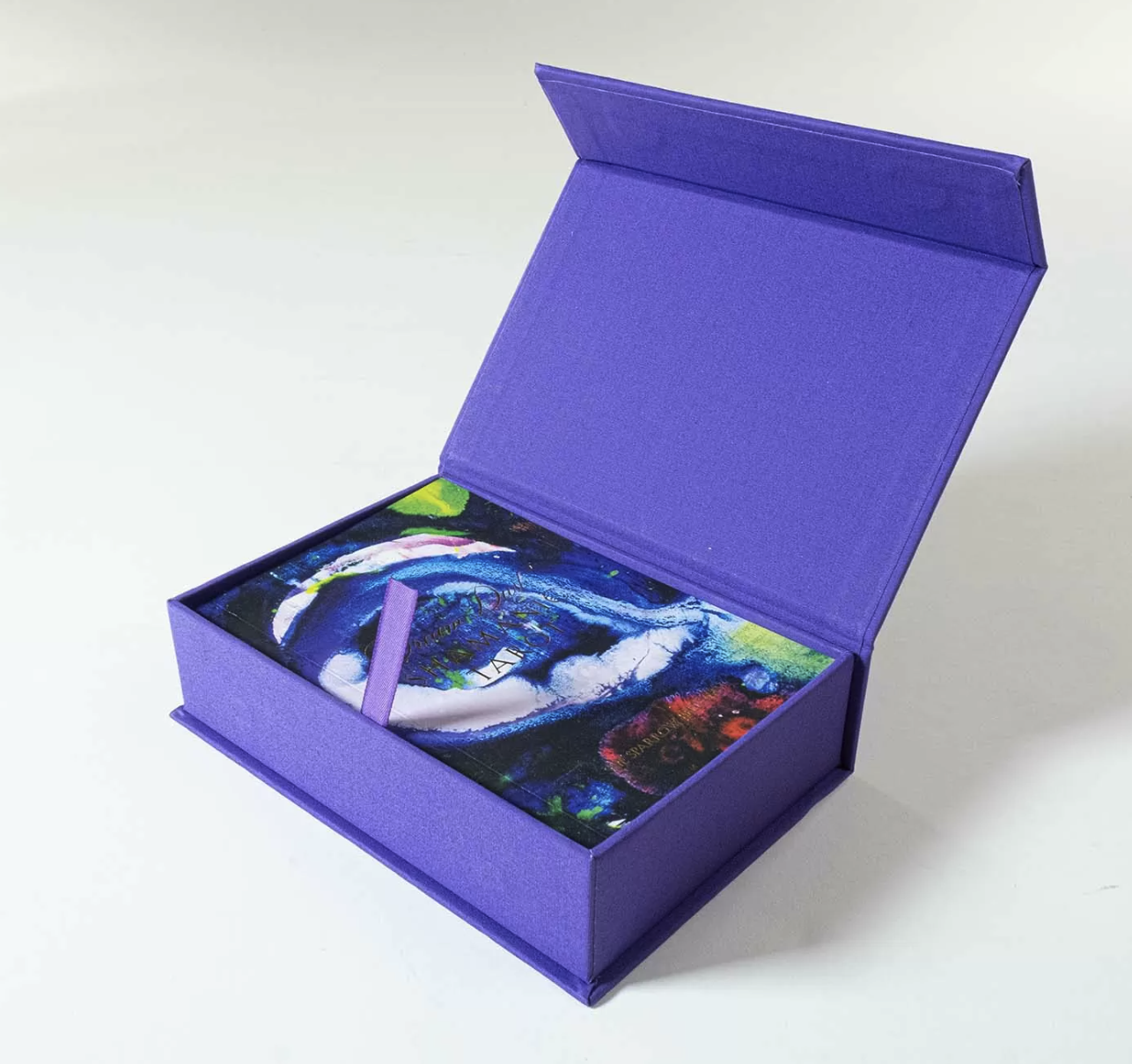 Photograph of a purple two-piece box with a magnetic-closure lid open to about 90 degrees, showing the printed lining inside the lid and a card visible in the bottom tray