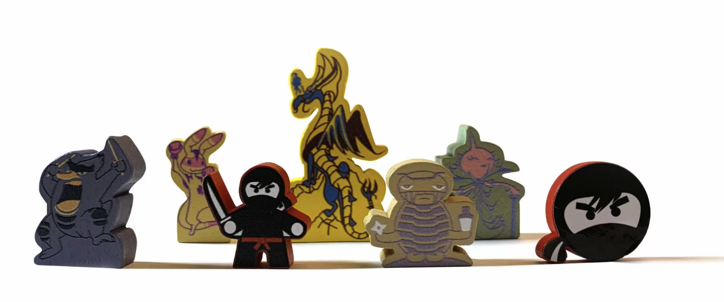 Photograph of five custom wooden game-piece meeples lined up: a stone-gargoyle figure, a robed character with a sword, a golden phoenix, a turtle, and a black ninja