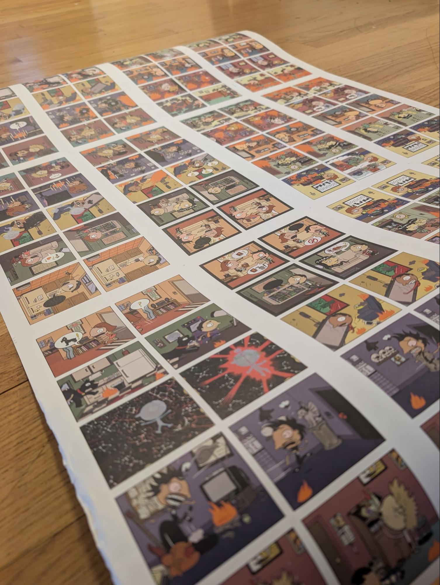 An uncut printed proof sheet laid on a wood floor, showing dozens of small comic panels arranged in a grid across the full sheet