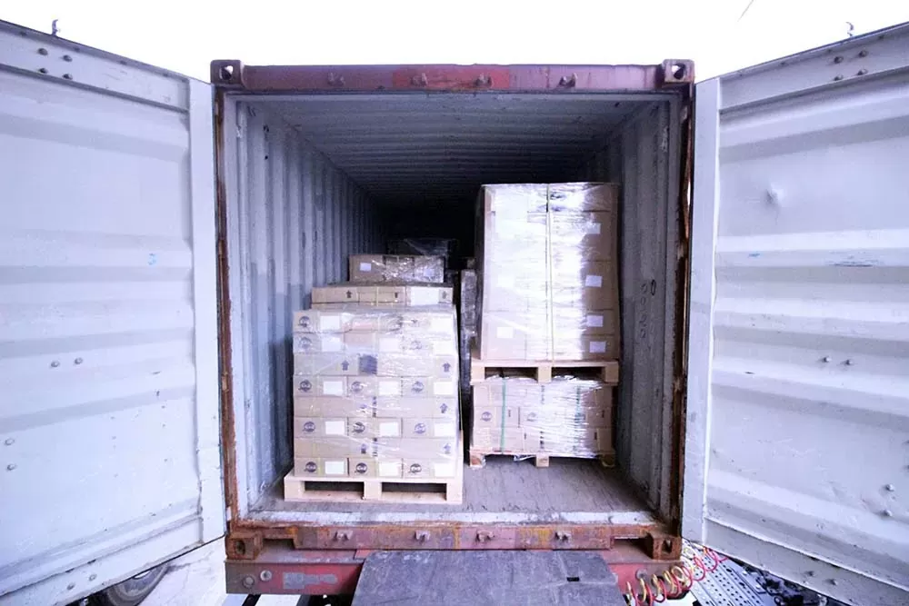 The open rear doors of a shipping container revealing neatly stacked palletized cartons loaded inside