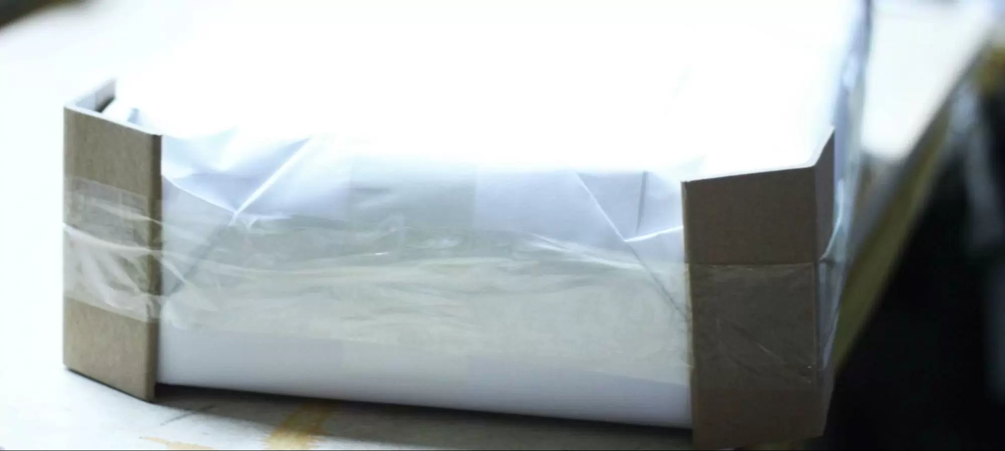 A close-up of books wrapped in clear plastic film with stiff cardboard corner protectors taped to each end of the stack