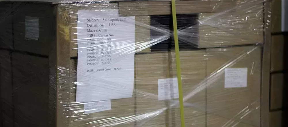 A pallet of cartons wrapped in clear stretch film and banded with a yellow strap, with a packing list reading Shipper 511 Capital LLC, Destination USA, Made in China, and a total carton count of 34 pieces